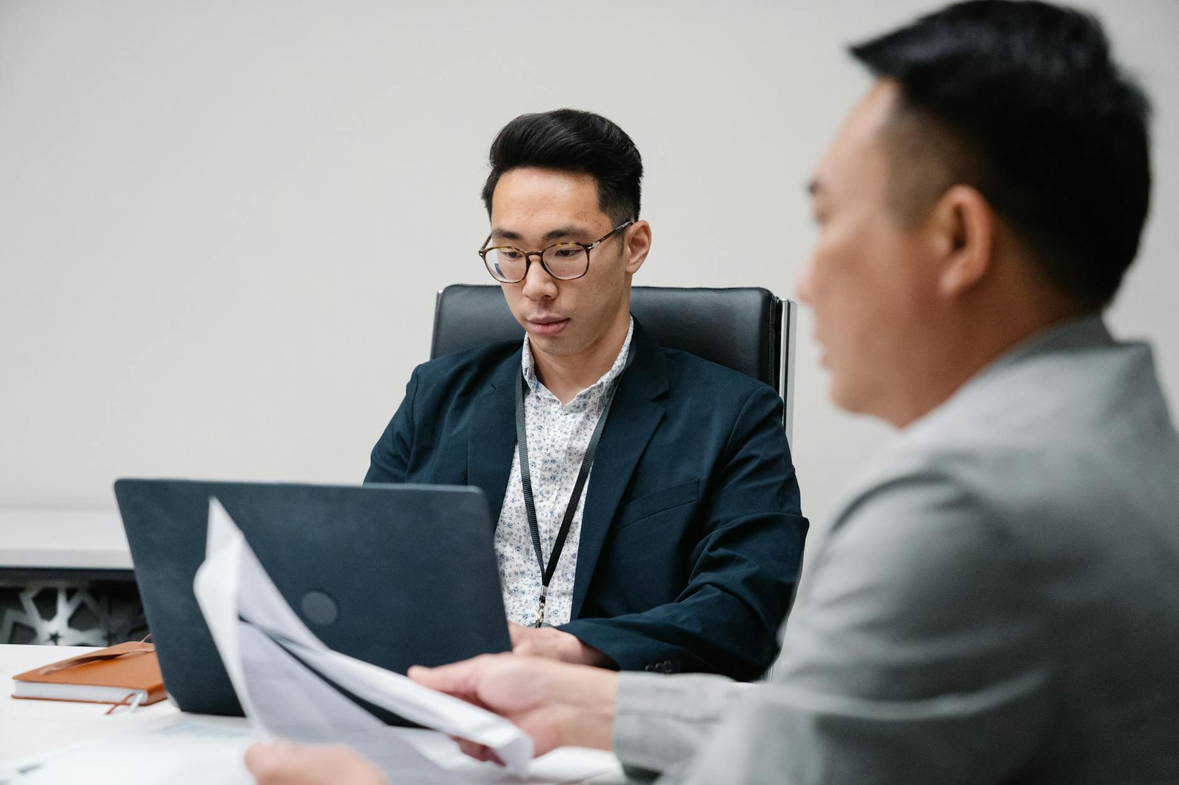 Two business professionals focused during a meeting, working on laptops and documents.