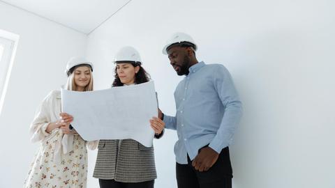 Group of professionals in hard hats examining construction blueprints indoors.