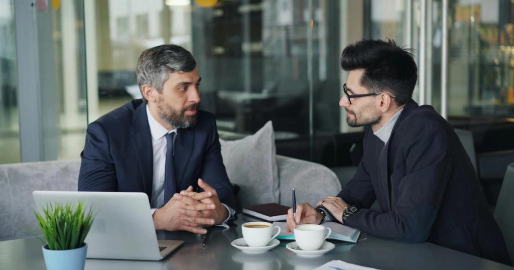 Two businessmen having a meeting with laptops, papers, and coffee at a modern office.