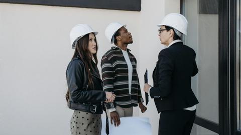A diverse group of professionals in construction helmets reviewing property plans outdoors.
