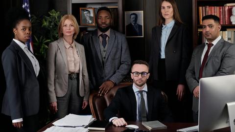 A diverse group of business professionals posing in an office, showcasing teamwork and leadership.