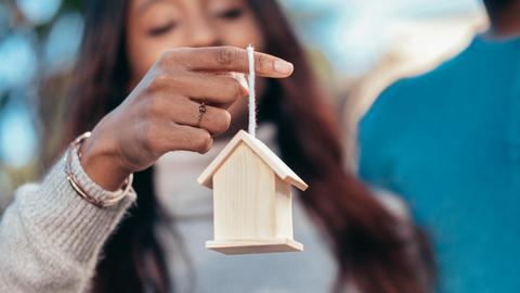 Close-up of a woman holding a wooden house symbolizing real estate or homeownership.