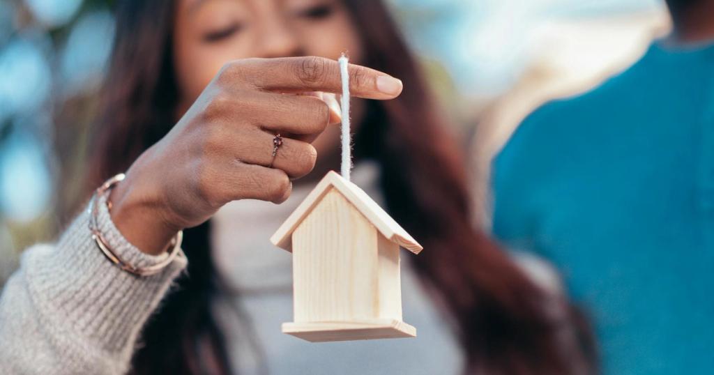 Close-up of a woman holding a wooden house symbolizing real estate or homeownership.