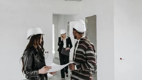 Diverse construction team in hard hats reviewing blueprints inside a building project.