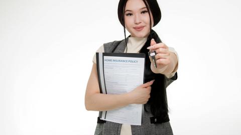Asian woman smiling while holding a home insurance policy and a key, symbolizing new home ownership.