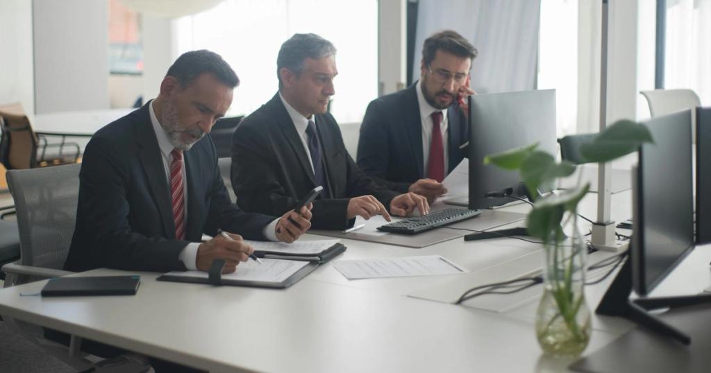 Three men in suits collaborating at a modern office desk with computers and documents.