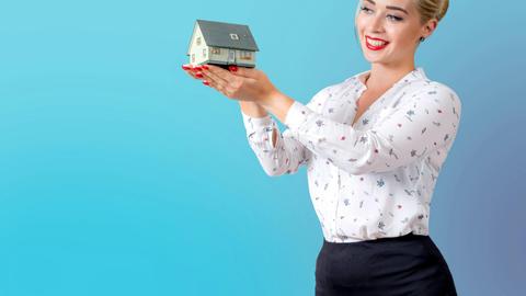 Professional woman in elegant attire holding a miniature house model, symbolizing real estate and home ownership.