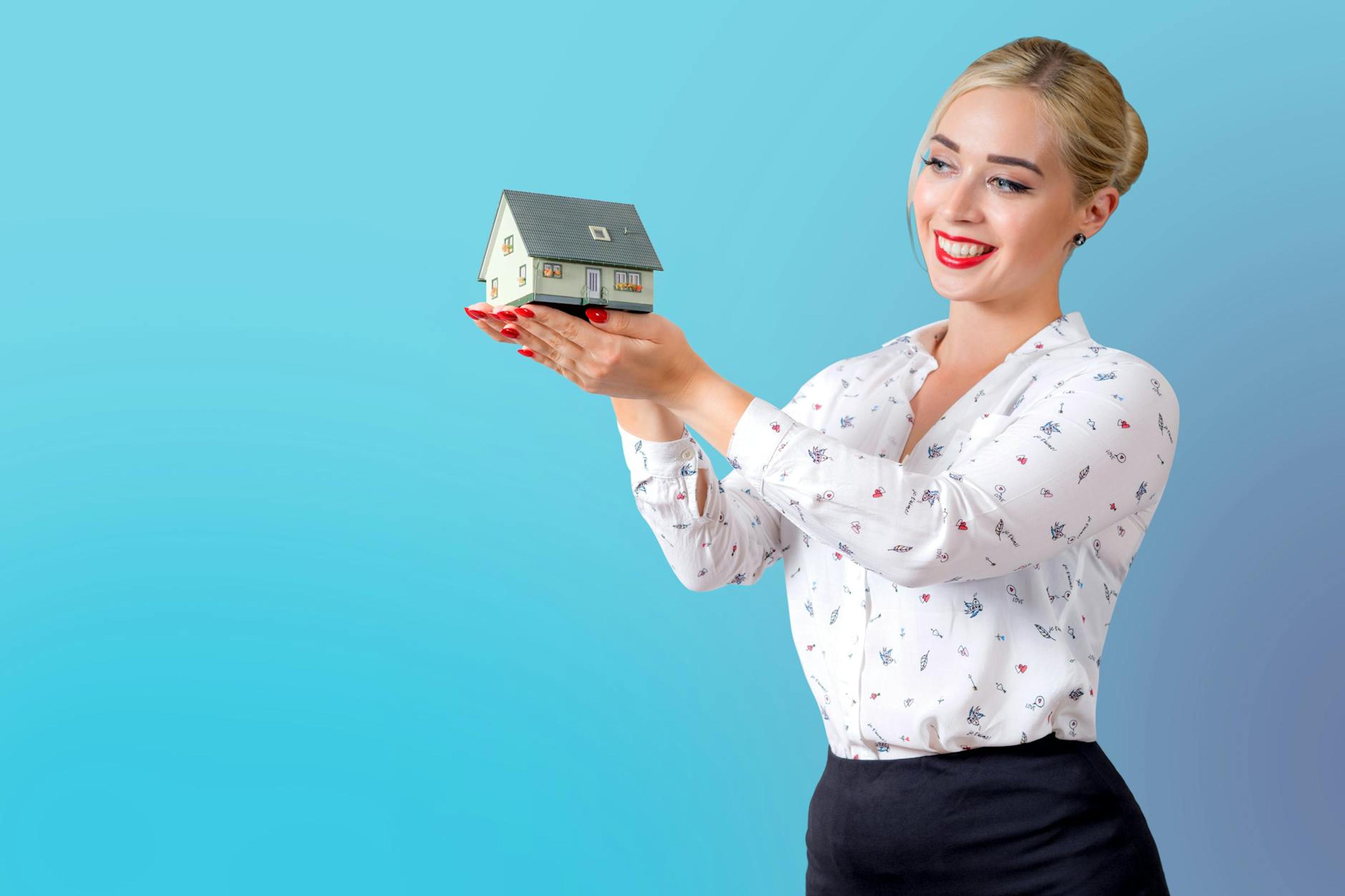 Professional woman in elegant attire holding a miniature house model, symbolizing real estate and home ownership.