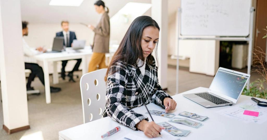 Focused businesswoman reviewing financial documents and currency in a modern office setting.