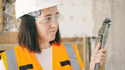 Caucasian woman in PPE holding a plumber's wrench indoors, focused on maintenance.