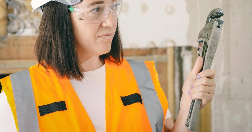 Caucasian woman in PPE holding a plumber's wrench indoors, focused on maintenance.