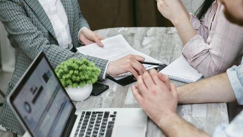 Professional meeting discussing business agreements with laptops and documents on a rustic table.