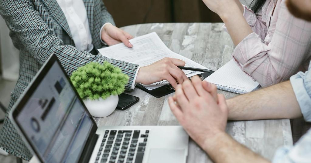 Professional meeting discussing business agreements with laptops and documents on a rustic table.