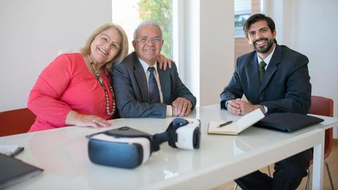 Elderly couple smiling with real estate agent during home meeting, showcasing modern technology.