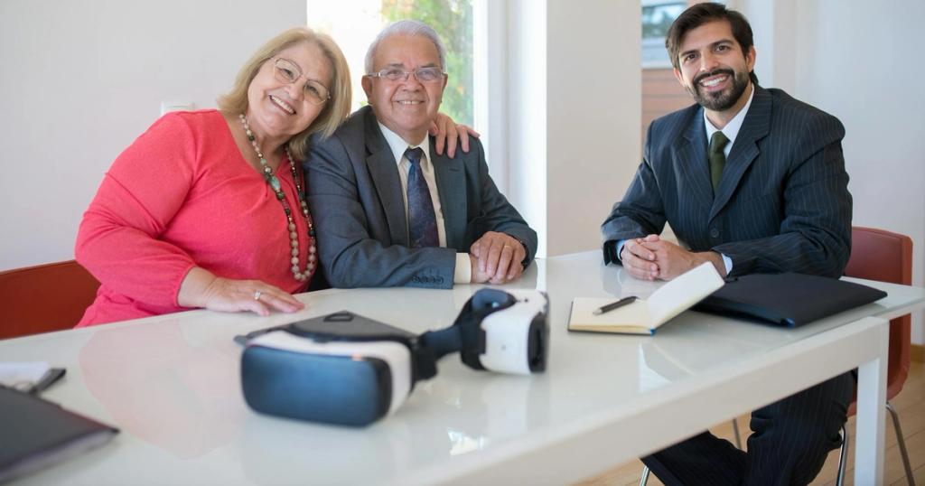 Elderly couple smiling with real estate agent during home meeting, showcasing modern technology.