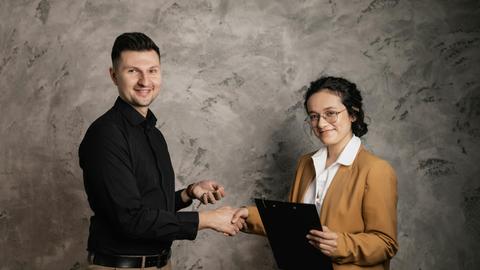 Man and woman shaking hands in a business agreement indoors, smiling confidently.