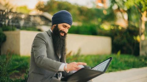 Man wearing business attire and turban reviews a portfolio outdoors, showcasing professionalism and focus.
