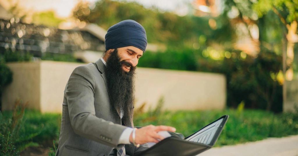Man wearing business attire and turban reviews a portfolio outdoors, showcasing professionalism and focus.