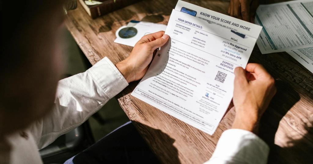 An adult man examining a financial document under natural light at a wooden desk, emphasizing finance and reading.
