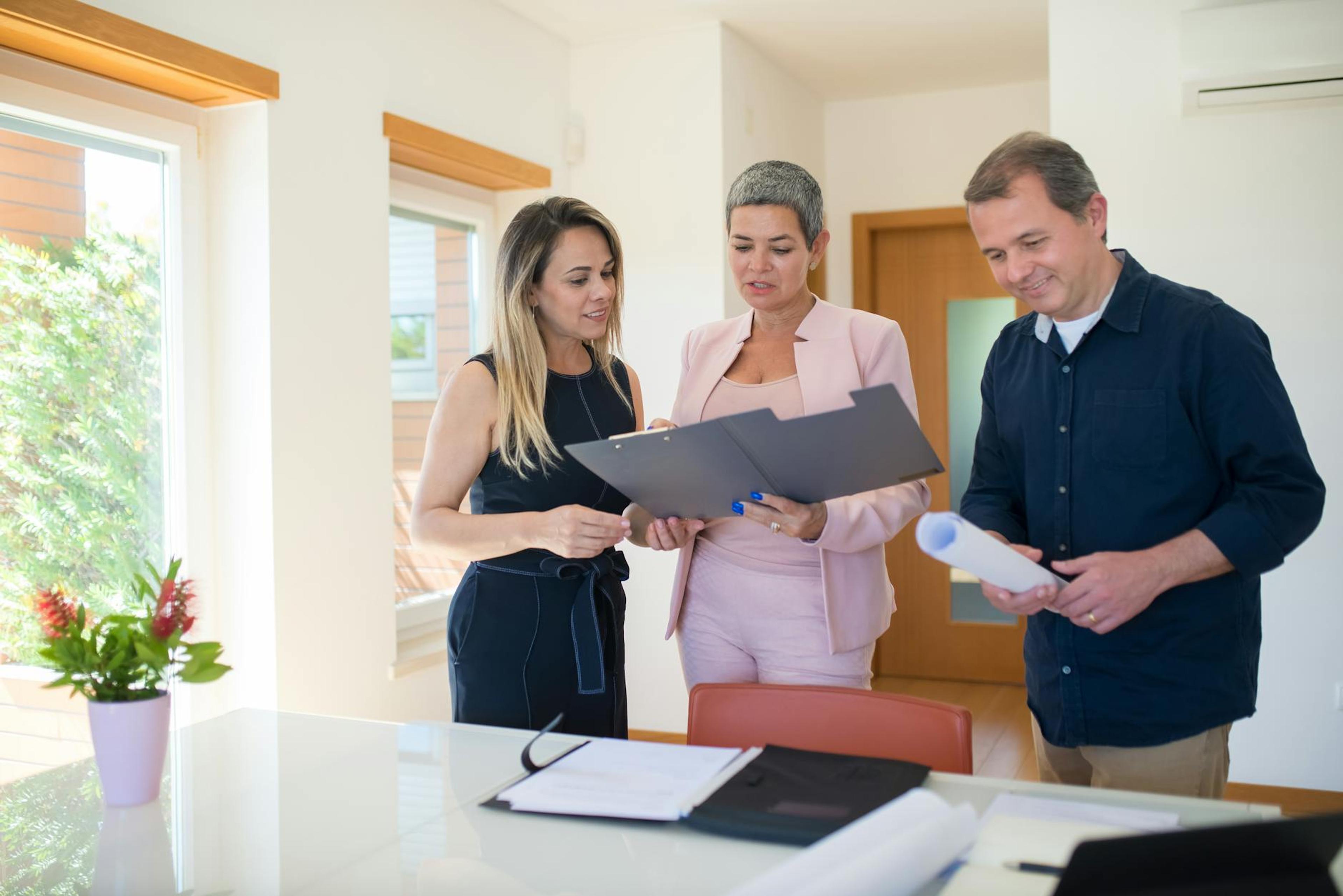 Three real estate professionals examining documents in a modern office setting, focusing on a property sale.