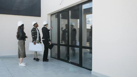 A diverse group of architects and a real estate agent examine a modern building, focusing on large glass windows.
