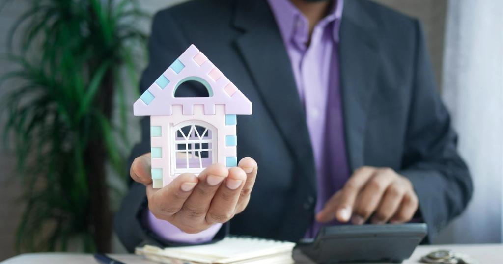 Businessman in suit holds model house, calculates real estate investments.