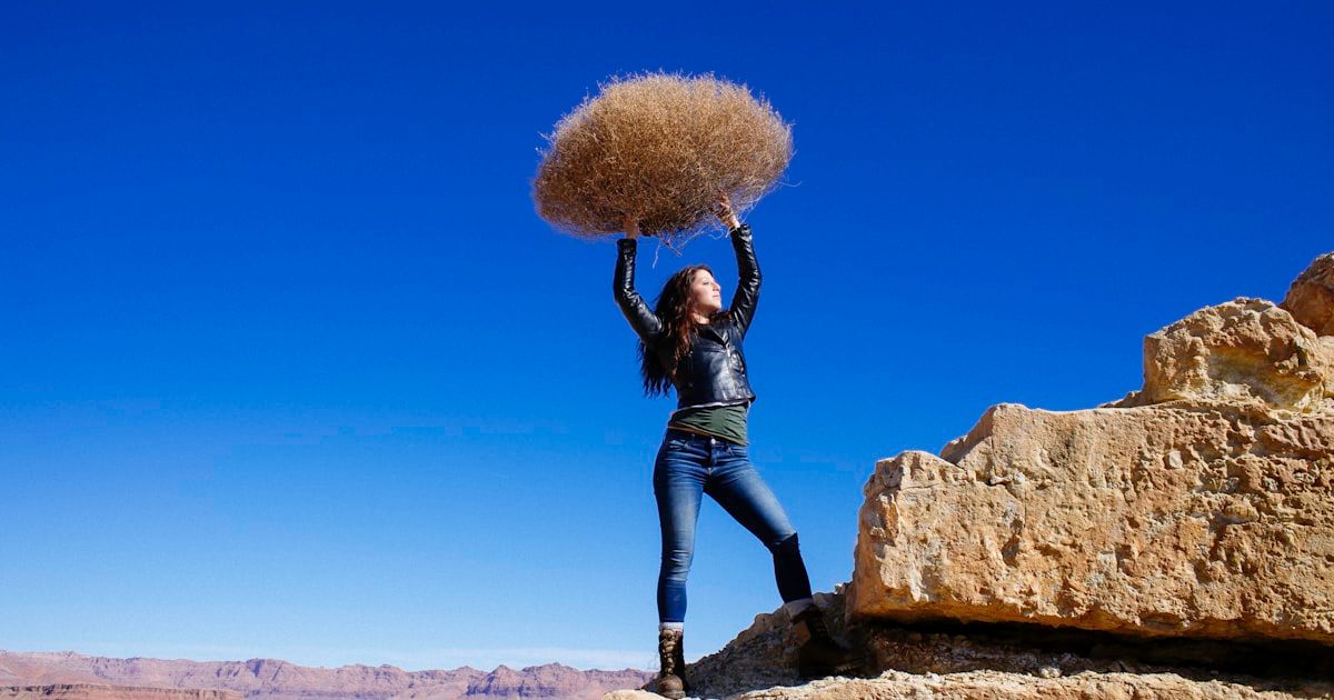 woman standing on rock formation while carrying hay during daytime