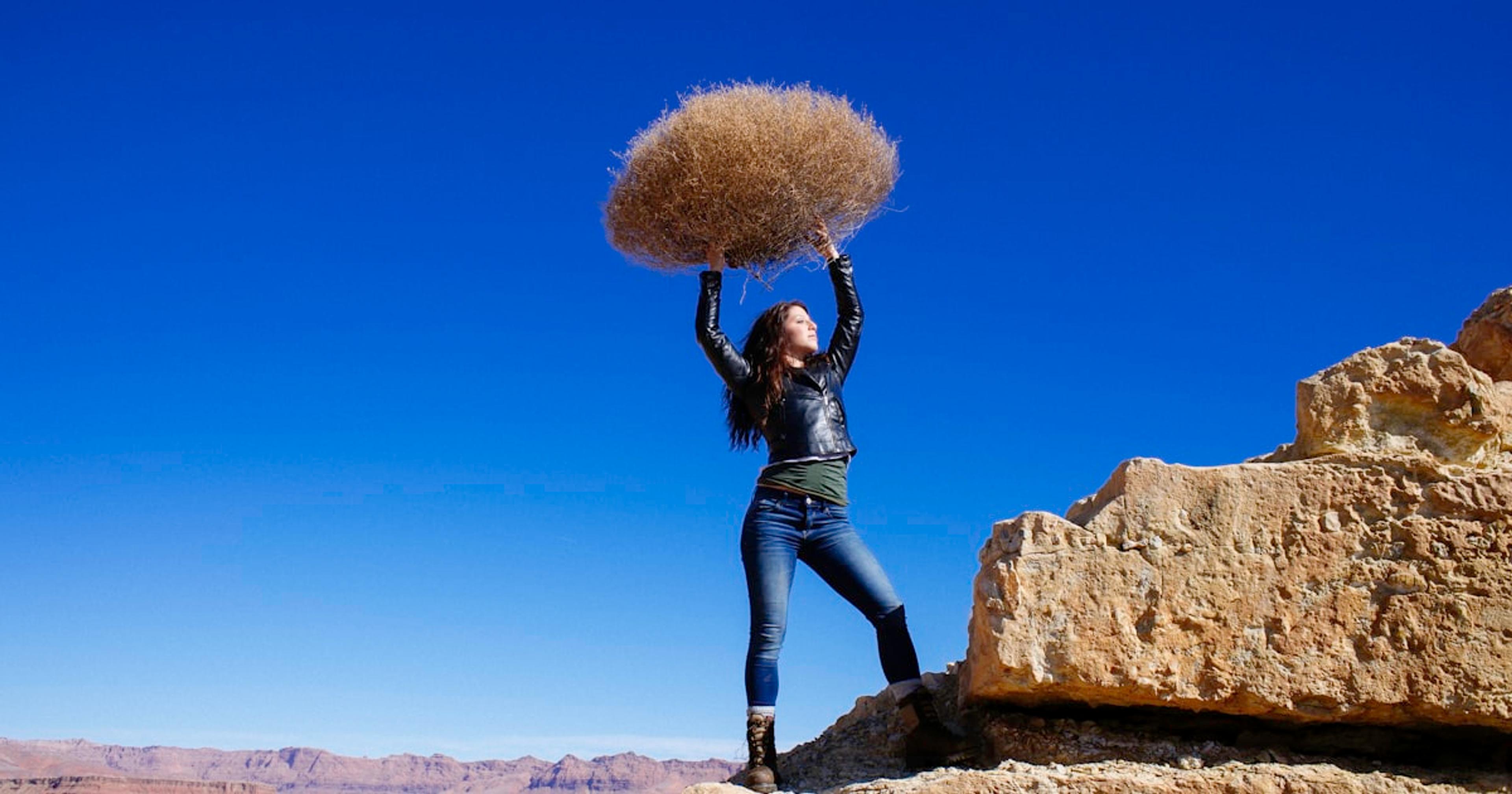 woman standing on rock formation while carrying hay during daytime