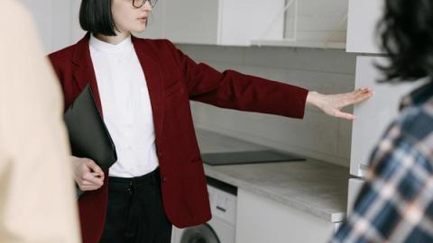 A female real estate agent demonstrates a modern kitchen to potential buyers in an apartment.