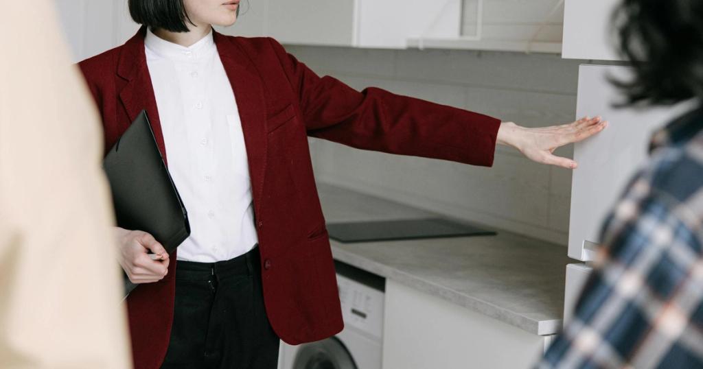 A female real estate agent demonstrates a modern kitchen to potential buyers in an apartment.