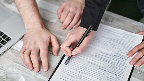 Close-up image of two people signing an insurance policy document on a wooden desk.