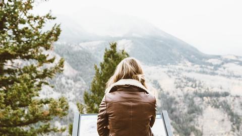back photo of woman wearing black leather jacket in front of snowed mountain