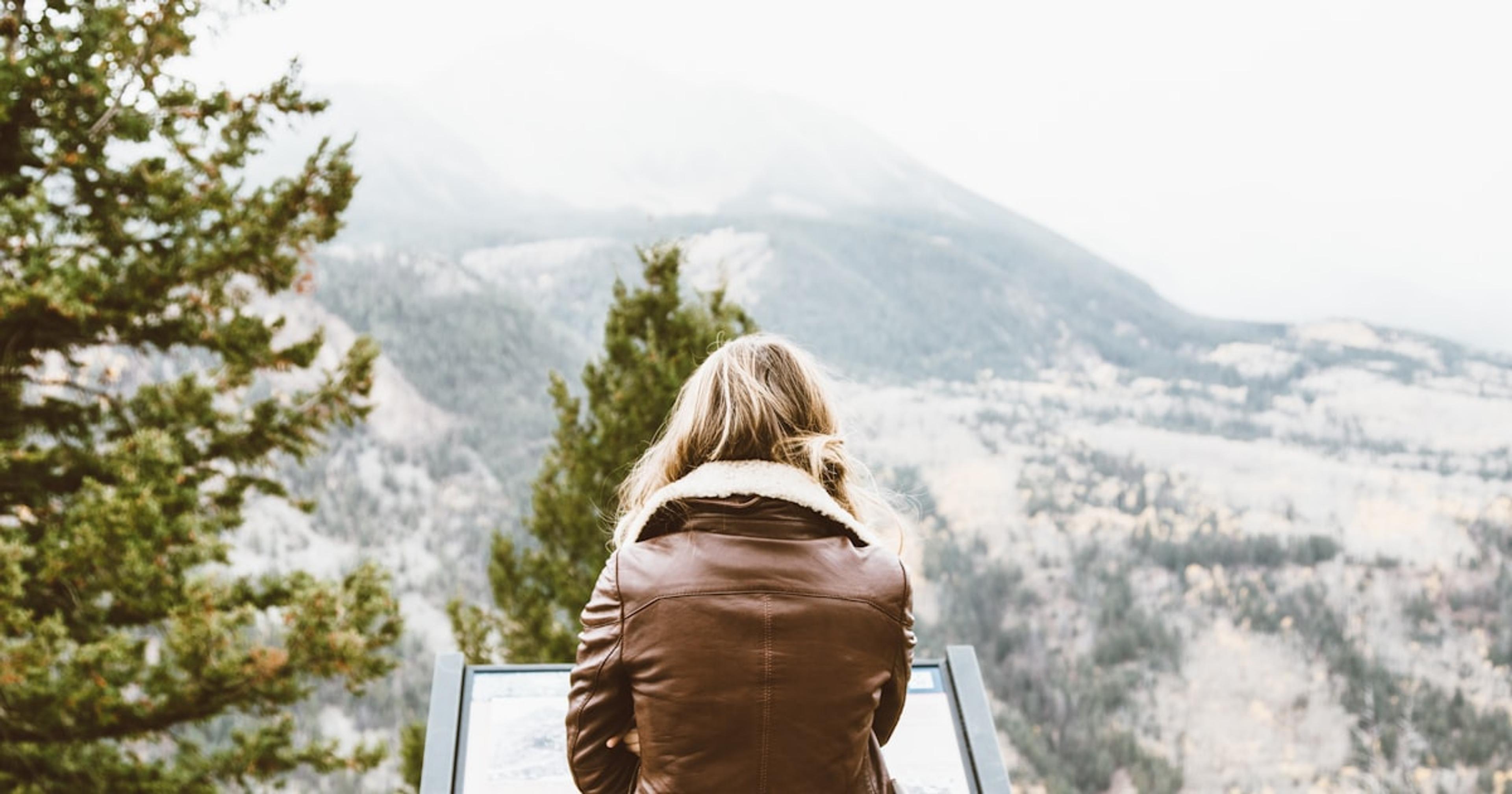 back photo of woman wearing black leather jacket in front of snowed mountain