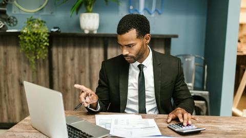 Professional man in a suit using a laptop and calculator in an office setting.