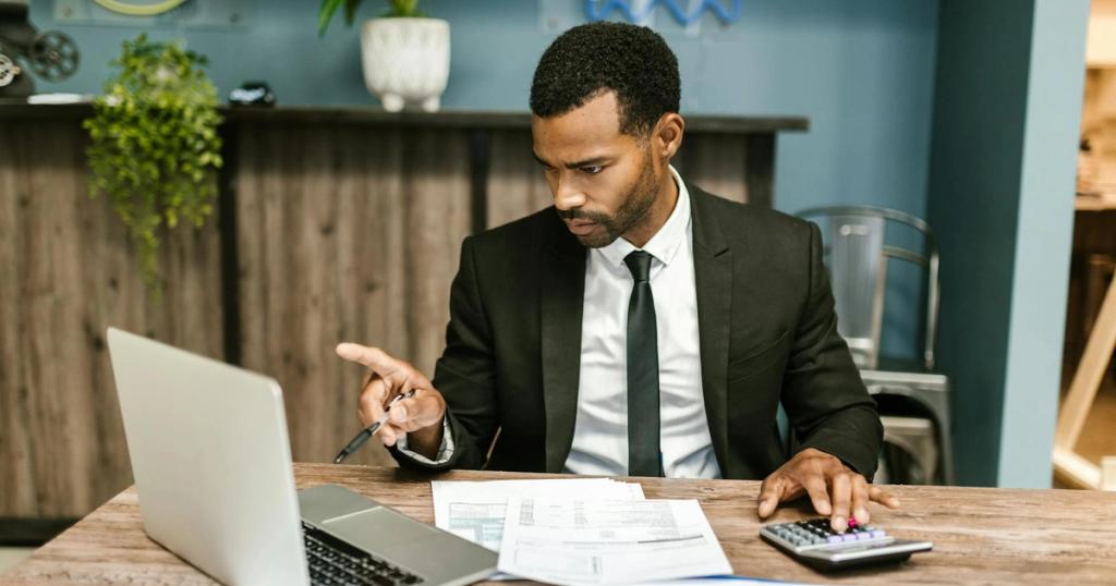 Professional man in a suit using a laptop and calculator in an office setting.