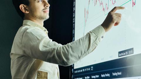 Man analyzing stock market graph on a digital board with a focused expression.