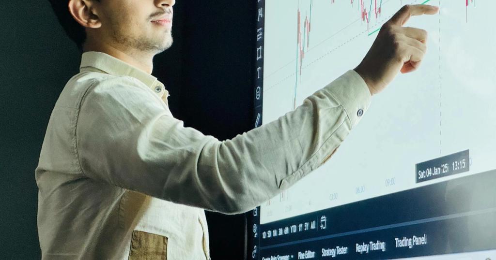 Man analyzing stock market graph on a digital board with a focused expression.