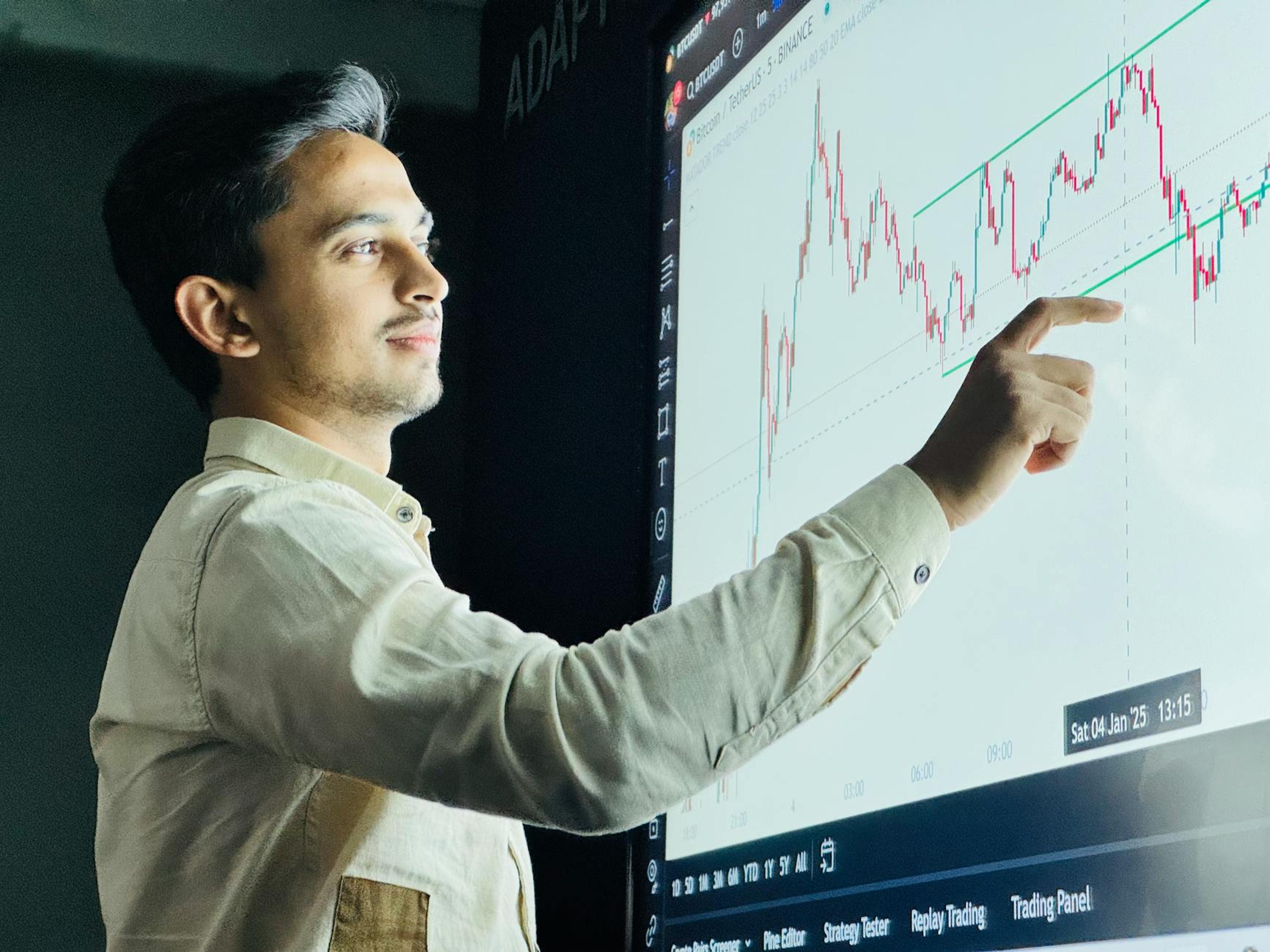 Man analyzing stock market graph on a digital board with a focused expression.