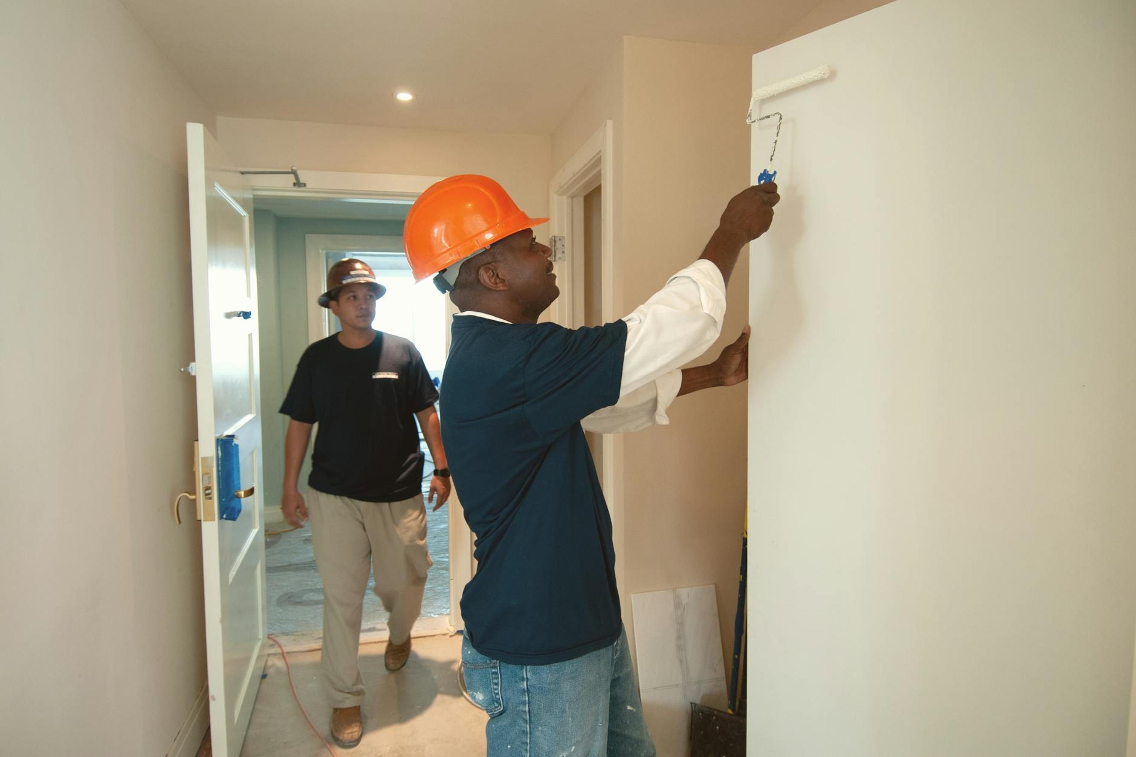 Two construction workers painting and renovating an interior. Focus on teamwork and home improvement.