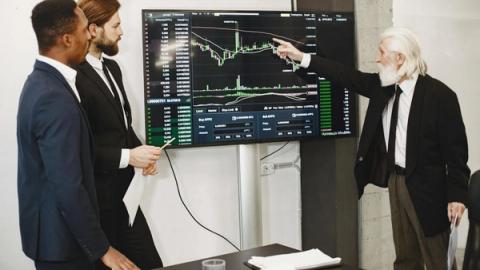 A diverse business team in a meeting analyzing stock market data on a screen.