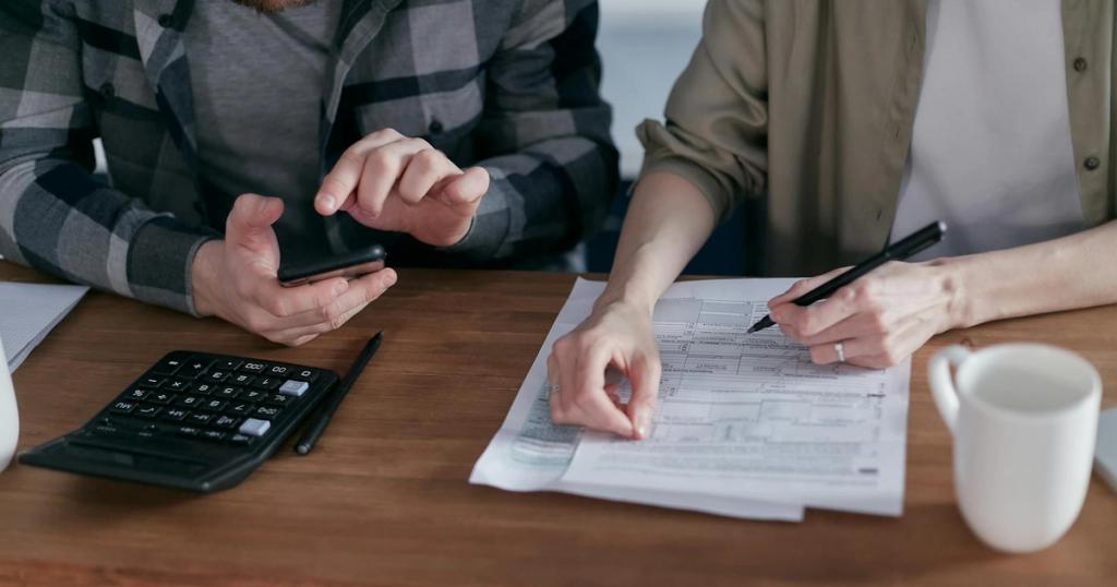 Two people working together on tax forms using a calculator at a wooden desk.