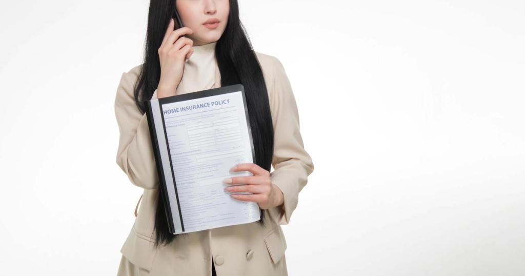 Asian woman in business attire holding home insurance policy while on a phone call.