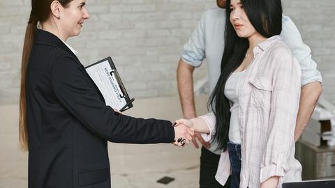 Professional business meeting with a handshake in an office environment featuring three adults in conversation.