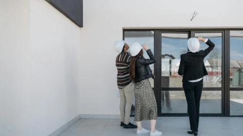 Three architects evaluating exterior building structure, wearing helmets and business attire.