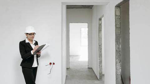 Woman architect in helmet and suit inspecting unfinished interior. White walls signify new construction.
