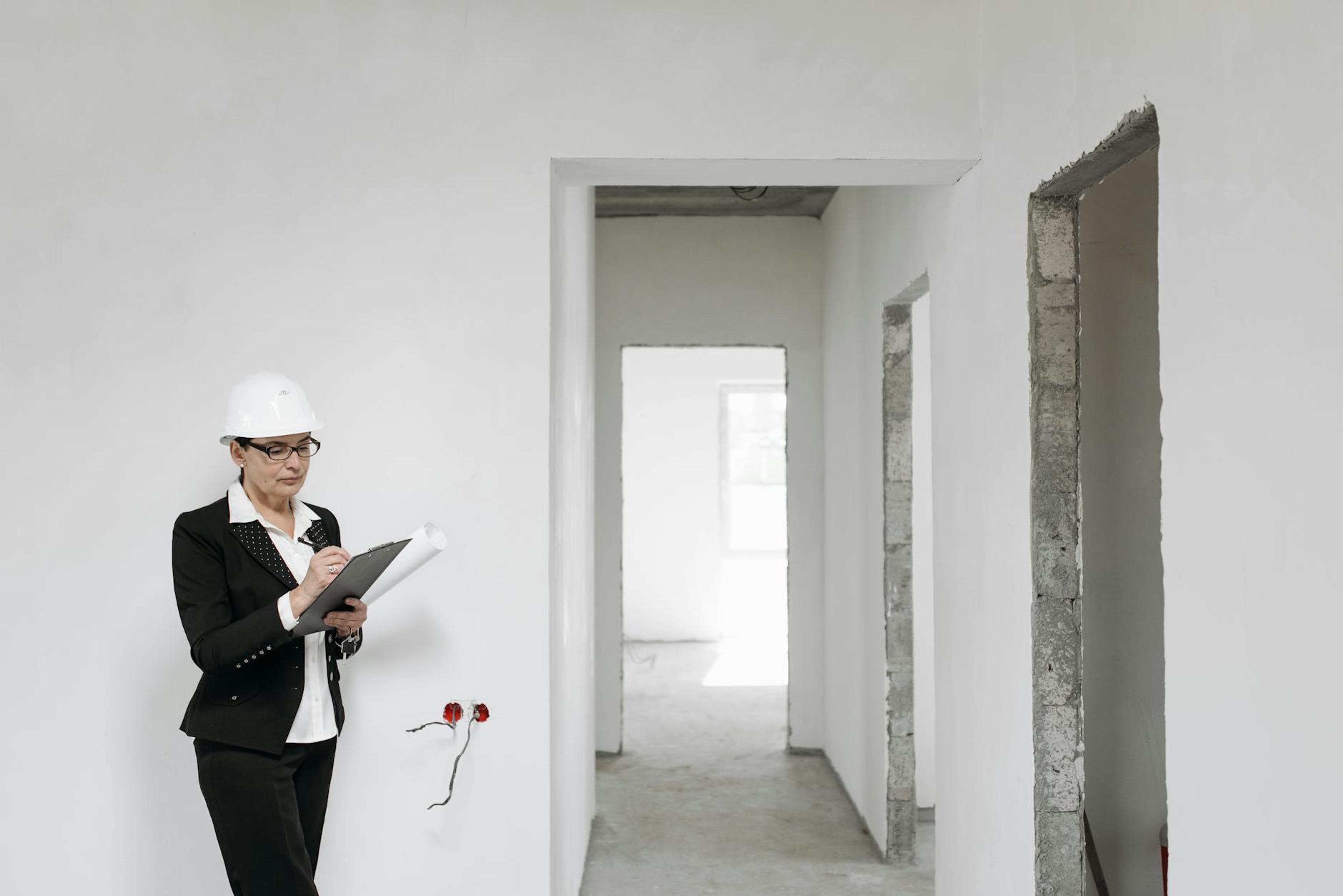 Woman architect in helmet and suit inspecting unfinished interior. White walls signify new construction.