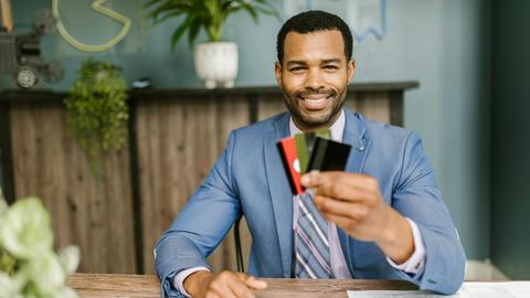 Smiling African American man in a suit holding credit cards at a business desk.