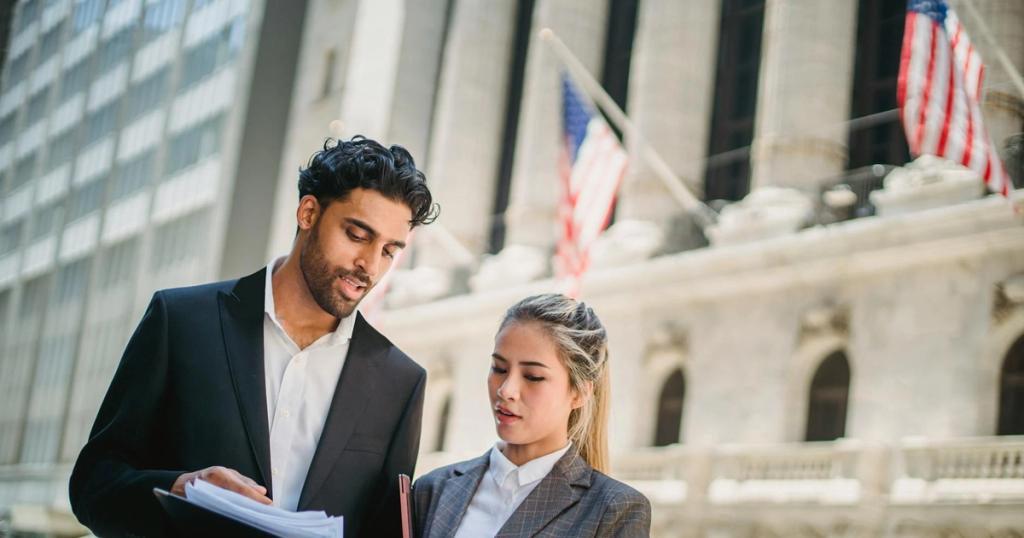 Two business professionals review documents outside a financial institution, indicating teamwork and collaboration.