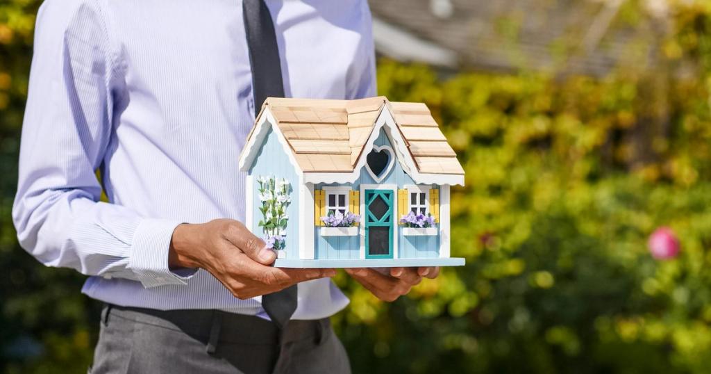 Businessman holds small house model outdoors, symbolizing real estate investment.