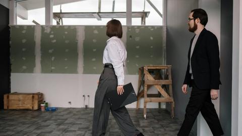 Businessman and businesswoman reviewing office construction progress indoors.